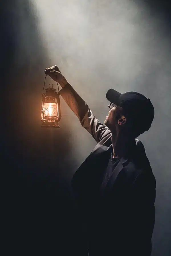 A lone man with a lantern in the smoke and darkness, searching forward as a symbol of guidance, courage, and inner truth way