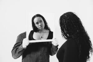 A woman looking into a mirror held by another person, reflecting self-awareness, perspective, and relational insight.