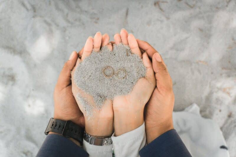 Two hands holding sand with wedding rings, symbolizing marriage counseling and commitment
