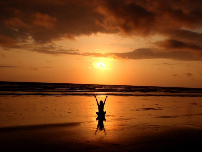 Person meditating on the beach at sunset, representing mindfulness and emotional well-being through work-life balance counselling in Singapore.
