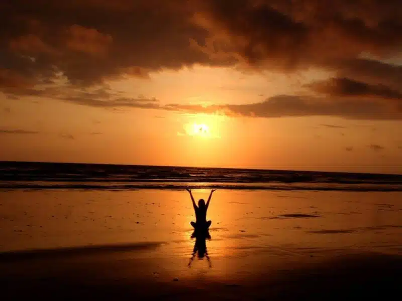 Person meditating on the beach at sunset, representing mindfulness and emotional well-being through work-life balance counselling in Singapore.