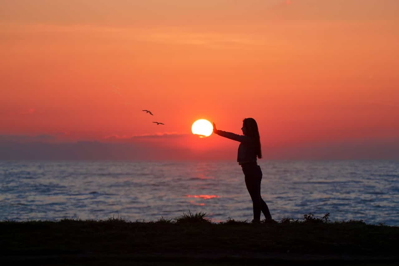 Silhouette of a woman holding the sun at sunset, symbolizing hope and emotional balance in anxiety therapy