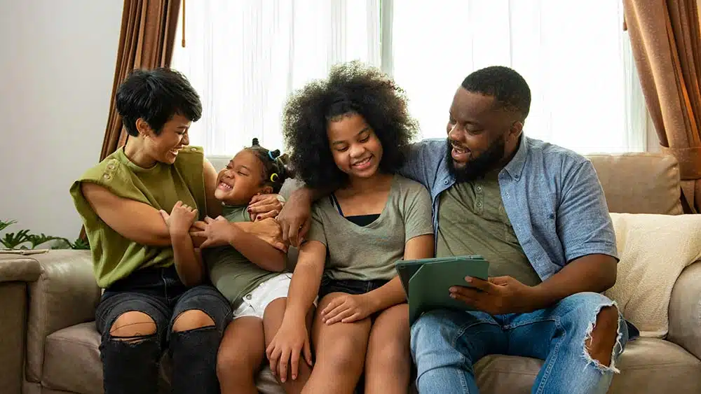 African mixed-race parents smiling with their two young daughters, enjoying time together as a family.