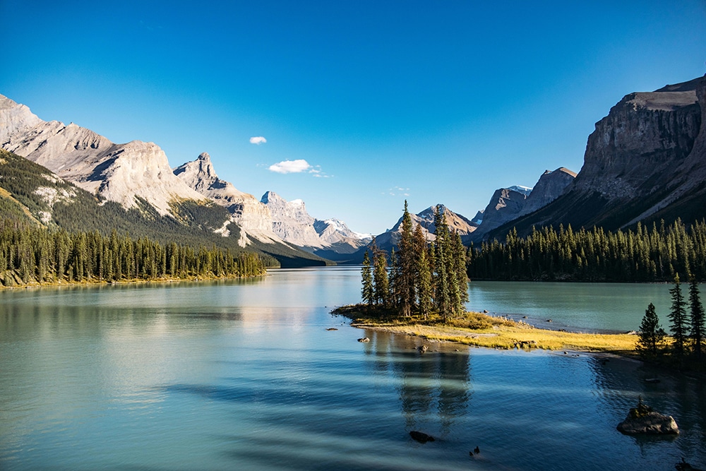 serene lake with a tree covered island surrounded by majestic mountains
