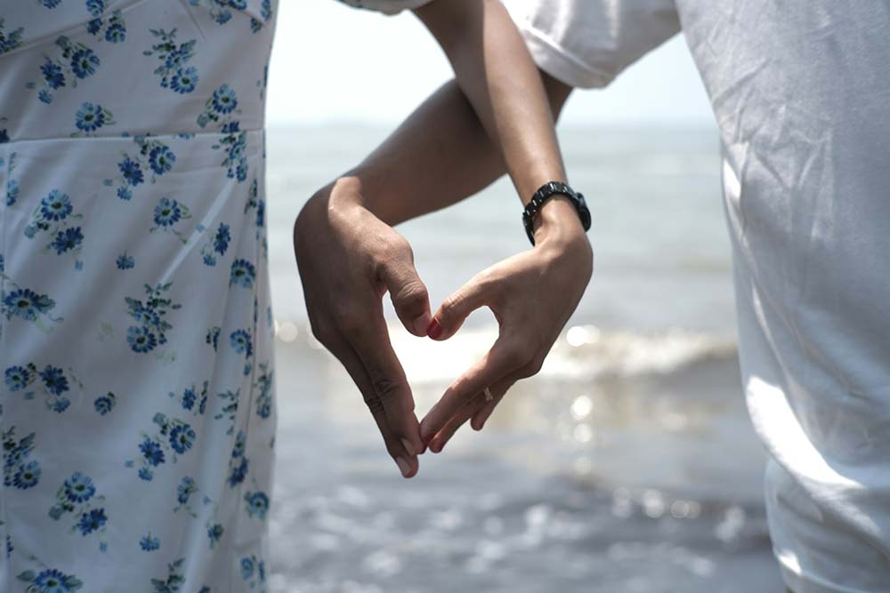 Couple forming a heart shape with hands at the beach